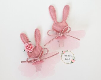 May include: Two pink bunny hair clips with tulle skirts and bows. One bunny has a pink flower on its head. The clips are labeled "Ruthies Bows".