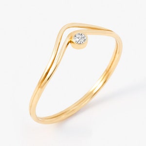 Pode incluir: Um anel de ouro com uma única gema pequena e transparente engastada no centro. O anel tem um design único de dupla banda que cria uma forma de V.