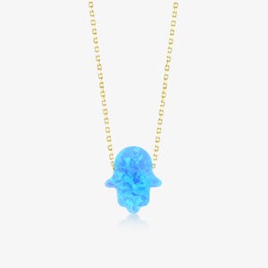 May include: A gold chain necklace featuring a bright blue hamsa hand pendant. The pendant has a vibrant, iridescent, and mottled texture throughout its surface, suspended from a delicate gold link chain that extends upwards from the top.