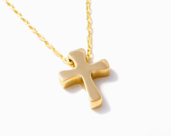 May include: A gold-toned metal cross pendant suspended from a matching delicate link chain. The cross features smooth, rounded edges and a polished surface, reflecting light across its curved form. The chain is thin with small, uniform links.