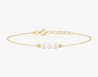 May include: A delicate gold chain bracelet featuring three centered white pearls and two small gold beads. The bracelet includes a lobster claw clasp and an adjustable extender chain with several circular links for a customizable fit.
