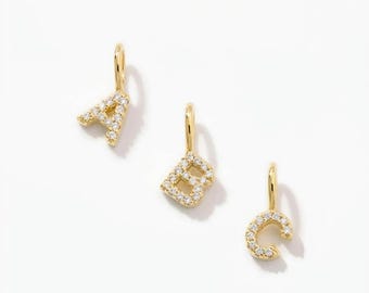 May include: Three gold-toned letter charms shaped as A, B, and C, each featuring a small bail at the top and embedded with tiny, clear, sparkling stones along the front surface of the letters, arranged diagonally against a plain white background.
