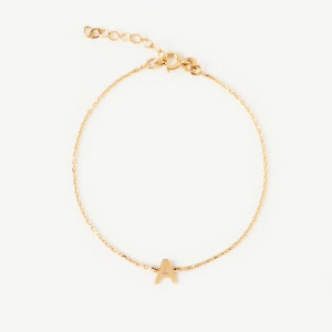 Könnte beinhalten: Ein goldenes Kettenarmband mit einem Buchstaben A-Anhänger.