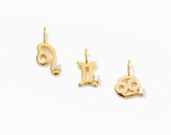 May include: Three gold-toned metal zodiac pendants, each featuring a small clear gemstone accent. The pendants represent the Leo, Gemini, and Cancer astrological symbols, and each includes a small circular loop at the top for attachment to a chain.