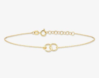 May include: A delicate gold chain bracelet featuring two interlocking circular links at the center. The bracelet includes a thin cable chain, a secure spring ring clasp, and a short extender chain with several small circular links for adjustment.