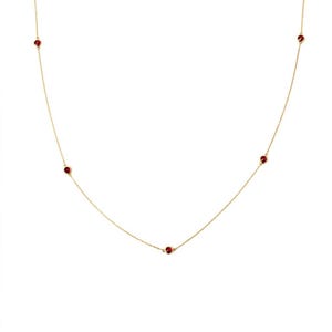 May include: A fine gold necklace with small, round, red gemstones set along the chain. The necklace is shown against a white backdrop, accentuating the contrast between the gold and the red stones. The necklace is a simple, elegant piece of jewellery.