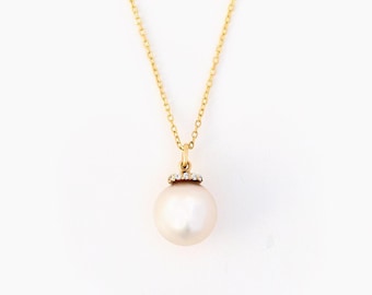 May include: A gold chain necklace featuring a round, white pearl pendant. The pearl is suspended from a small gold bail that is accented with a row of tiny, clear, sparkling stones at the top, connecting the pendant to the delicate gold link chain.