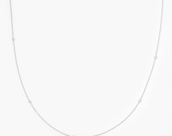 May include: A delicate silver-toned chain necklace featuring small, evenly spaced circular accents along its length. The thin metal links form a continuous, graceful curve, creating a simple and refined piece of jewelry with a polished finish.