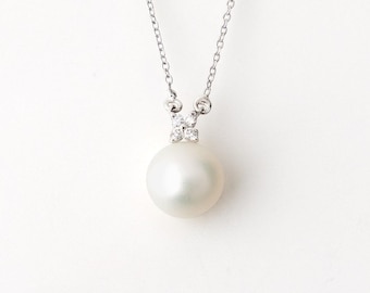 May include: A silver-toned necklace featuring a single round white pearl pendant suspended from a delicate chain. The pearl is topped with a small, four-petaled floral-shaped setting encrusted with four tiny, clear, sparkling stones.