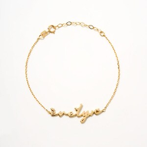 Könnte beinhalten: Ein goldenes Kettenarmband mit dem Namen "evelyn" in Kursivschrift.