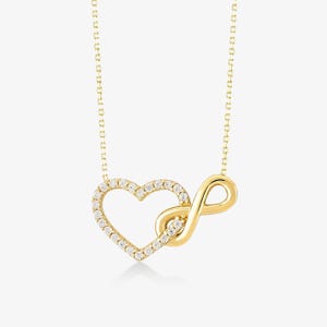 May include: A gold-toned necklace featuring a pendant that combines an open heart shape and an infinity symbol. The heart outline is encrusted with small, clear, sparkling stones, while the infinity loop is smooth, polished gold-toned metal.