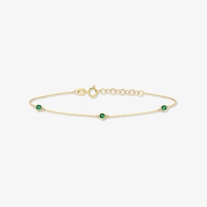May include: A delicate gold chain bracelet featuring three evenly spaced, round, bezel-set green gemstones. The bracelet includes a thin, polished gold link chain and a secure circular spring ring clasp with an adjustable extension chain at the end.
