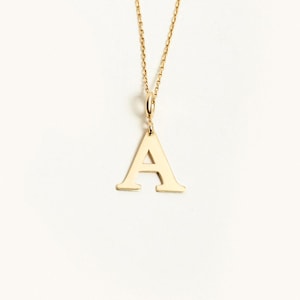 May include: A gold-toned necklace featuring a capital letter A pendant suspended from a delicate chain. The pendant has a polished, smooth surface and a classic serif font style. The chain is thin and connects to the top of the letter pendant.