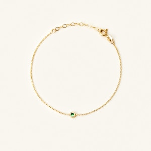 May include: A delicate gold chain bracelet with a single green gemstone.