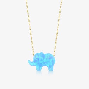 May include: A delicate gold chain necklace featuring a pendant shaped like an elephant. The elephant pendant is crafted from a bright blue synthetic opal material with a mottled, iridescent surface texture that reflects light in various shades.