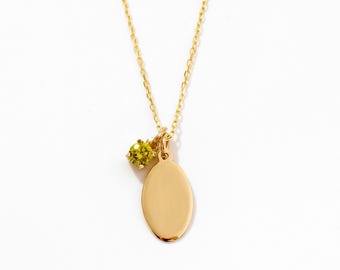May include: A gold chain necklace featuring a small, smooth, oval-shaped pendant and a single, round, faceted chartreuse-colored gemstone charm suspended from the same jump ring, creating a delicate and polished jewelry piece.