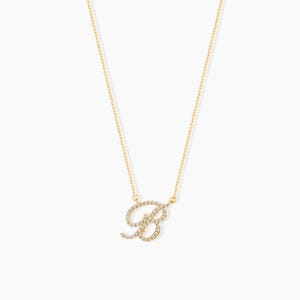 May include: A delicate gold necklace featuring the letter "B" encrusted with small, sparkling gemstones. The pendant hangs from a fine gold chain, creating a simple yet elegant piece of jewelry. The necklace is displayed against a plain white background.