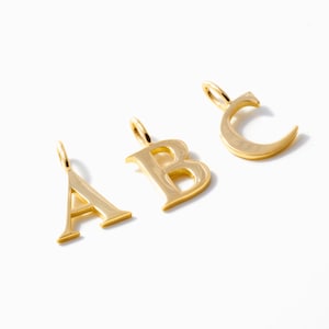 May include: Three gold-coloured alphabet pendants spelling out "A", "B", and "C". Each letter has a small loop at the top for a chain. The pendants are displayed on a white background.