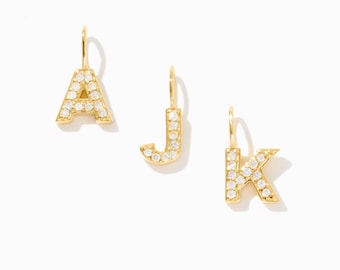 May include: Three gold-toned letter charms shaped as A, J, and K. Each letter features a polished gold finish and is embedded with small, clear, round-cut stones along the front surface. Each charm includes a small vertical gold loop at the top.