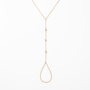 May include: A gold-toned hand chain featuring a delicate cable chain design. The piece includes a central vertical chain segment adorned with three small, evenly spaced gold beads, terminating in a teardrop-shaped loop for the finger.