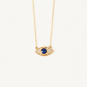 May include: A gold chain necklace with a blue sapphire eye charm surrounded by clear cubic zirconia stones.