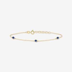 Op de afbeelding: Een delicate gouden kettingarmband met drie kleine blauwe edelstenen.