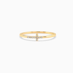 May include: A thin gold ring featuring a small cross design on the front. The cross is embellished with seven tiny, clear, round-cut stones set into the metal. The band is smooth, polished, and circular, maintaining a consistent width throughout.