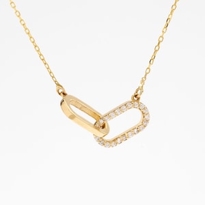 May include: A gold chain necklace featuring two interlocking oval links as a pendant. One link is plain polished gold, while the other is encrusted with small, clear, round-cut stones along its entire outer surface, suspended from a delicate chain.