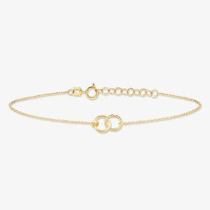 May include: A delicate gold chain bracelet featuring two interlocking circular links at the center. One link has a smooth polished finish, while the other features a textured twisted design. The bracelet includes a spring ring clasp and an adjustable chain.