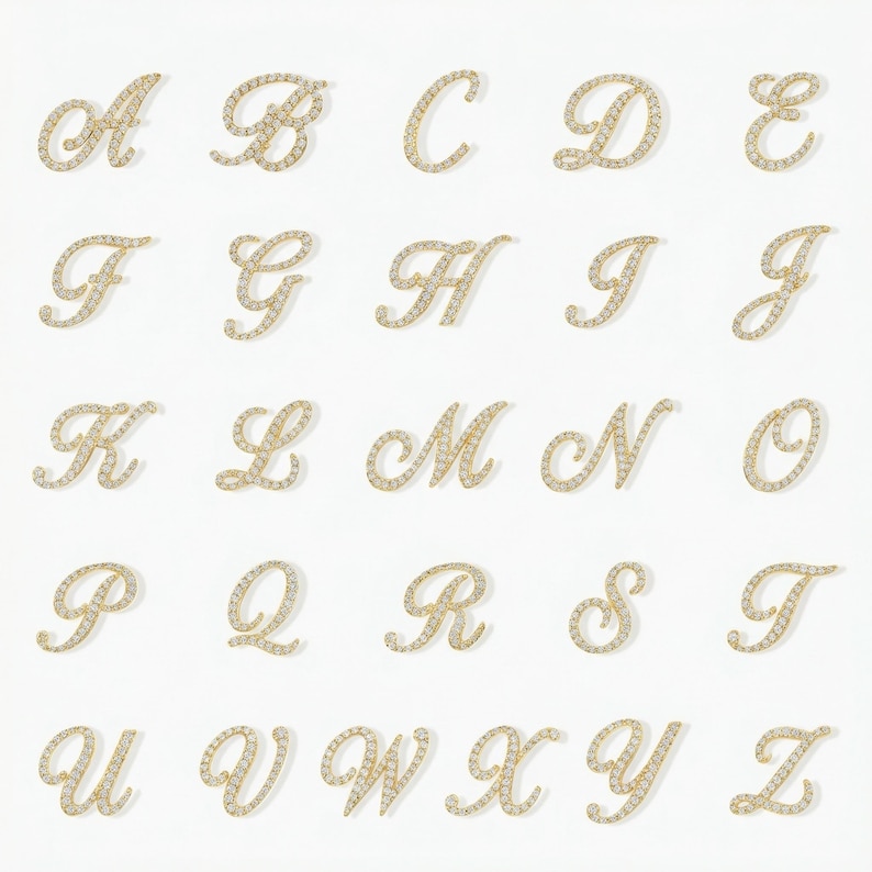 May include: A collection of gold-colored, cursive letter charms, each encrusted with small, sparkling stones. The letters A through Z are displayed against a white background. The charms are arranged in rows and columns.