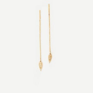 May include: A pair of gold threader earrings featuring a delicate, elongated chain design. Each earring terminates in a small, flat, leaf-shaped charm with a cut-out pattern, suspended from a thin, flexible gold chain that hangs vertically.