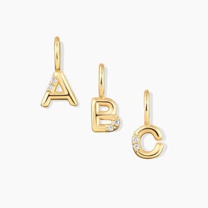 May include: Three gold-toned letter pendants shaped as A, B, and C. Each pendant features a small vertical bail at the top and is accented with two tiny, clear, round-cut stones embedded into the surface of the metal letters.