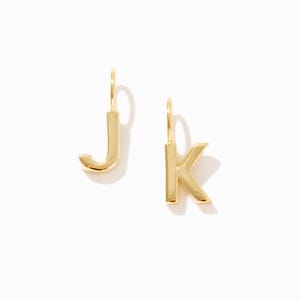 May include: Two gold-toned metal charms shaped like the letters J and K. Each letter features a smooth, polished surface and a small vertical loop at the top for attachment. The letters are rendered in a simple, clean, sans-serif typeface design.