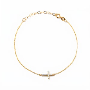 May include: A delicate gold bracelet featuring a sideways cross pendant adorned with small, sparkling gemstones. The bracelet has an adjustable chain and a secure clasp. The jewelry is set against a clean, white background.