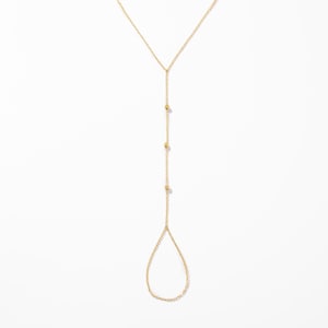 May include: A gold-toned chain hand harness featuring a delicate Y-shaped design. The piece consists of a thin chain that extends from a wrist section, adorned with three small evenly spaced gold beads, leading down to a teardrop-shaped finger loop.