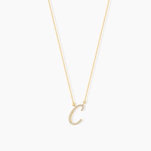 May include: A delicate gold-colored necklace featuring the letter "C" encrusted with small, sparkling gemstones. The pendant hangs from a fine chain, creating a simple yet elegant design. The necklace is displayed against a plain white background.