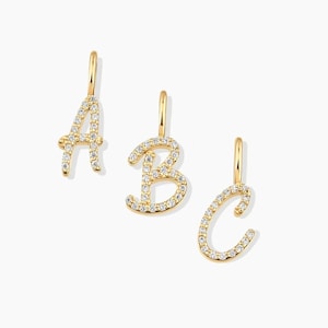May include: Three gold letter pendants shaped as A, B, and C, each featuring a cursive script design encrusted with small, clear, sparkling stones. Each pendant includes a small gold bail at the top for attachment to a chain or necklace.