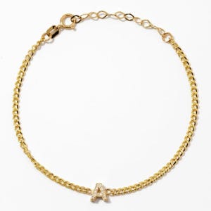 May include: A gold chain bracelet featuring a single letter A charm encrusted with small clear stones. The bracelet is constructed with interlocking oval links and includes a lobster claw clasp at the end of an adjustable chain extension.