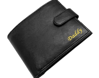 May include: A black bi-fold wallet with a textured surface and a snap-button closure strap. The word Daddy is printed in a yellow cursive font on the front right side of the wallet, which features visible stitching along the edges.