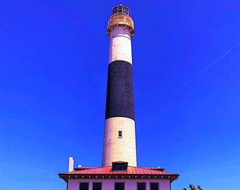 Puede incluir: Un faro con rayas blancas y negras, techo rojo y molduras blancas. El faro está rodeado por una valla de metal negro y arbustos verdes.