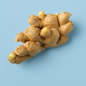 May include: A fresh, whole ginger root with a light brown, textured exterior and pale yellow tips. The ginger is set against a solid light blue background, showcasing its natural form and color.