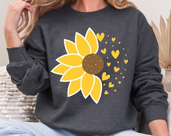 Könnte beinhalten: Dunkelgraues Sweatshirt mit einem großen gelben Sonnenblumen-Design, brauner Mitte und weißer Umrandung. Kleine gelbe Herzen sind rechts von der Sonnenblume verstreut. Bequemer, lässiger Stil.