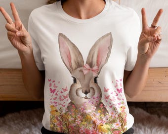 Puede incluir: Camiseta blanca con una ilustración de acuarela de un conejito con un lazo rosa y orejas largas. El conejito está rodeado de mariposas rosas y flores coloridas. Una prenda casual para el día a día.