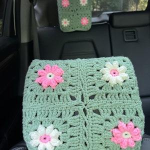 May include: Two crocheted headrest cushions for car seats. The cushions are green with white and pink flowers.
