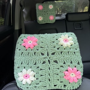 May include: Green crocheted car seat headrest with pink and white flower accents.