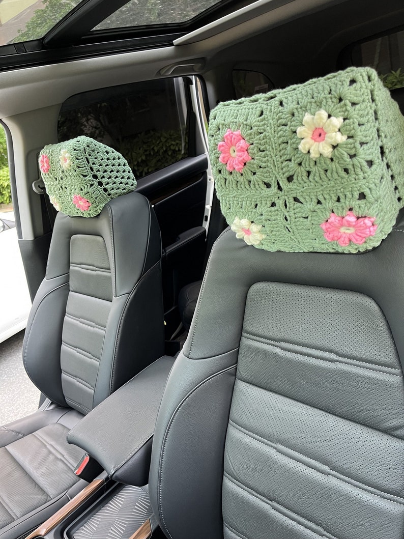 May include: Two crocheted headrest covers with a floral design in shades of green, pink, and white. The covers are placed on the headrests of two car seats.