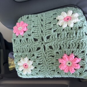 May include: A crocheted green car seat headrest cover with pink and white flowers.