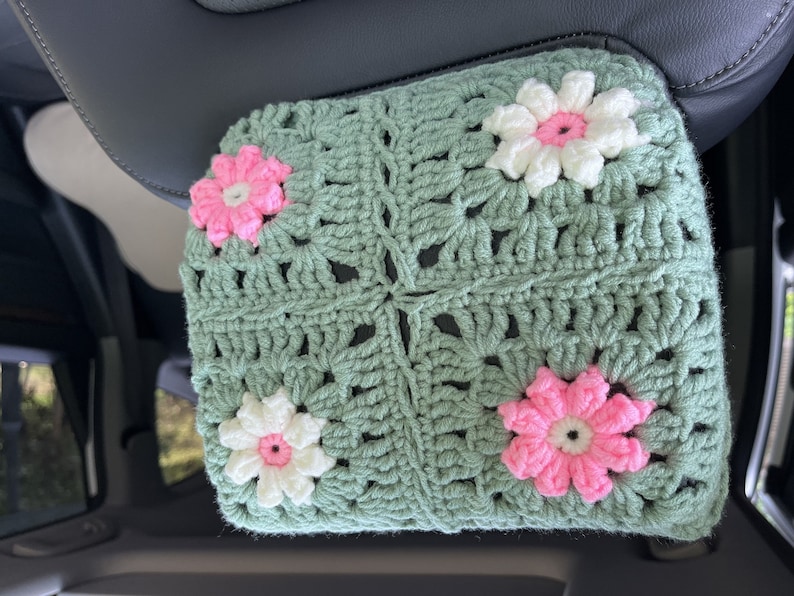 May include: A crocheted green car seat headrest cover with pink and white flowers.
