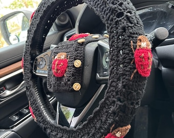 May include: Black crochet steering wheel cover and matching console cover, adorned with red and brown ladybug appliqués. The covers are handmade and add a unique, decorative touch to a car's interior.