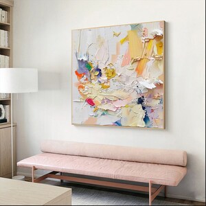 Op de afbeelding: Abstract schilderij met een witte achtergrond en kleurrijke penseelstreken in tinten roze, geel, blauw, groen en oranje. Het schilderij heeft een textuur en is ingelijst in een licht houten lijst.